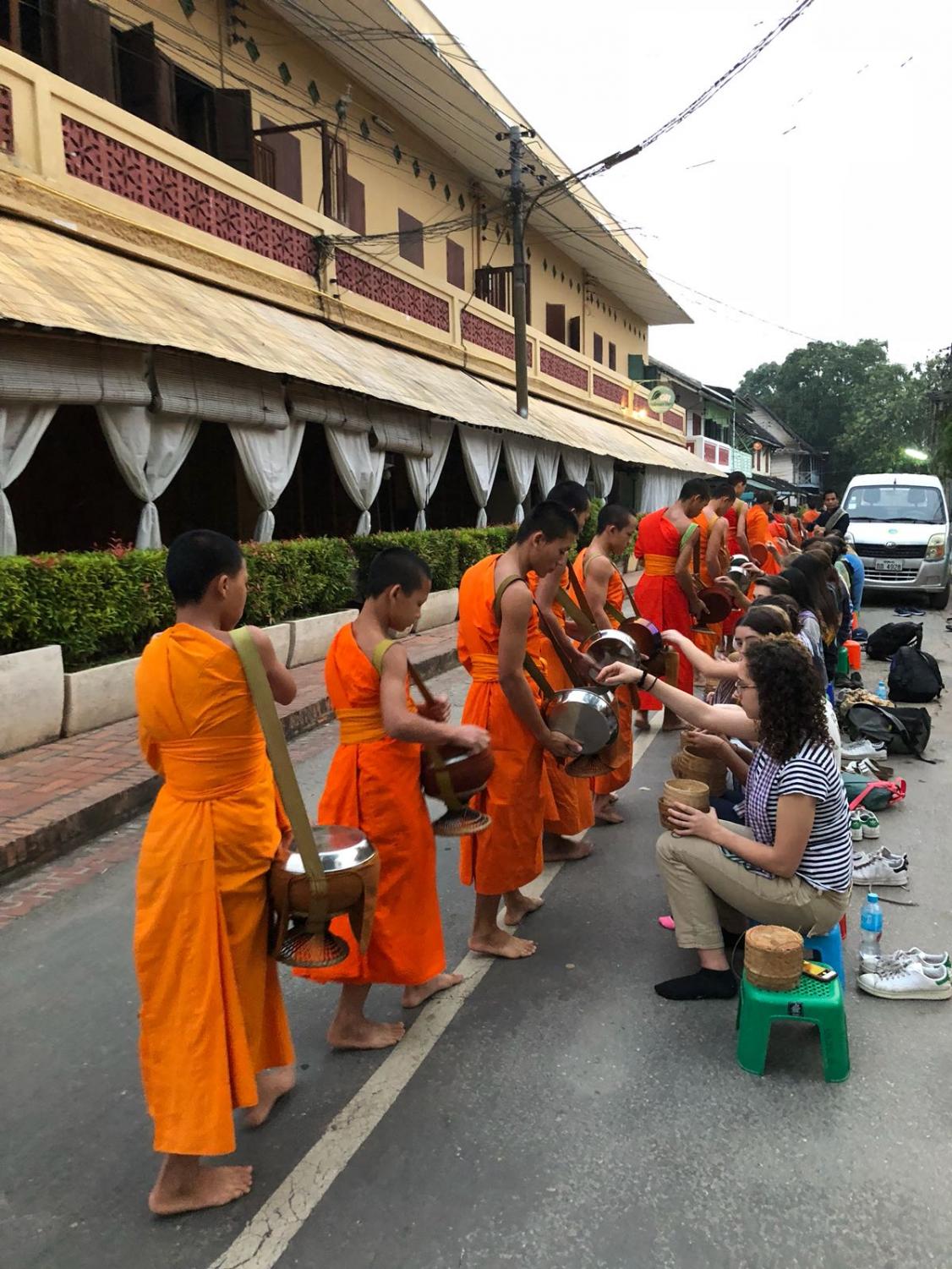 Students participate in the early morning Alms Giving Ceremony in Luang Prabang, Laos. In this ceremony, local Buddhist monks with alms bowls by their sides walk through the streets of Luang Prabang to receive food donations, most commonly steamed rice.