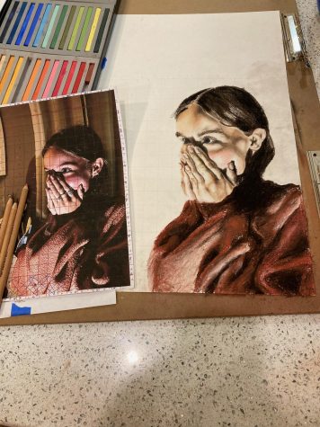 Sophie was also drawing another portrait for her sustained investigation work. She depicts a girl covering her mouth with her hands. She also has several supplies like pencils and pastels to help form her piece of artwork.