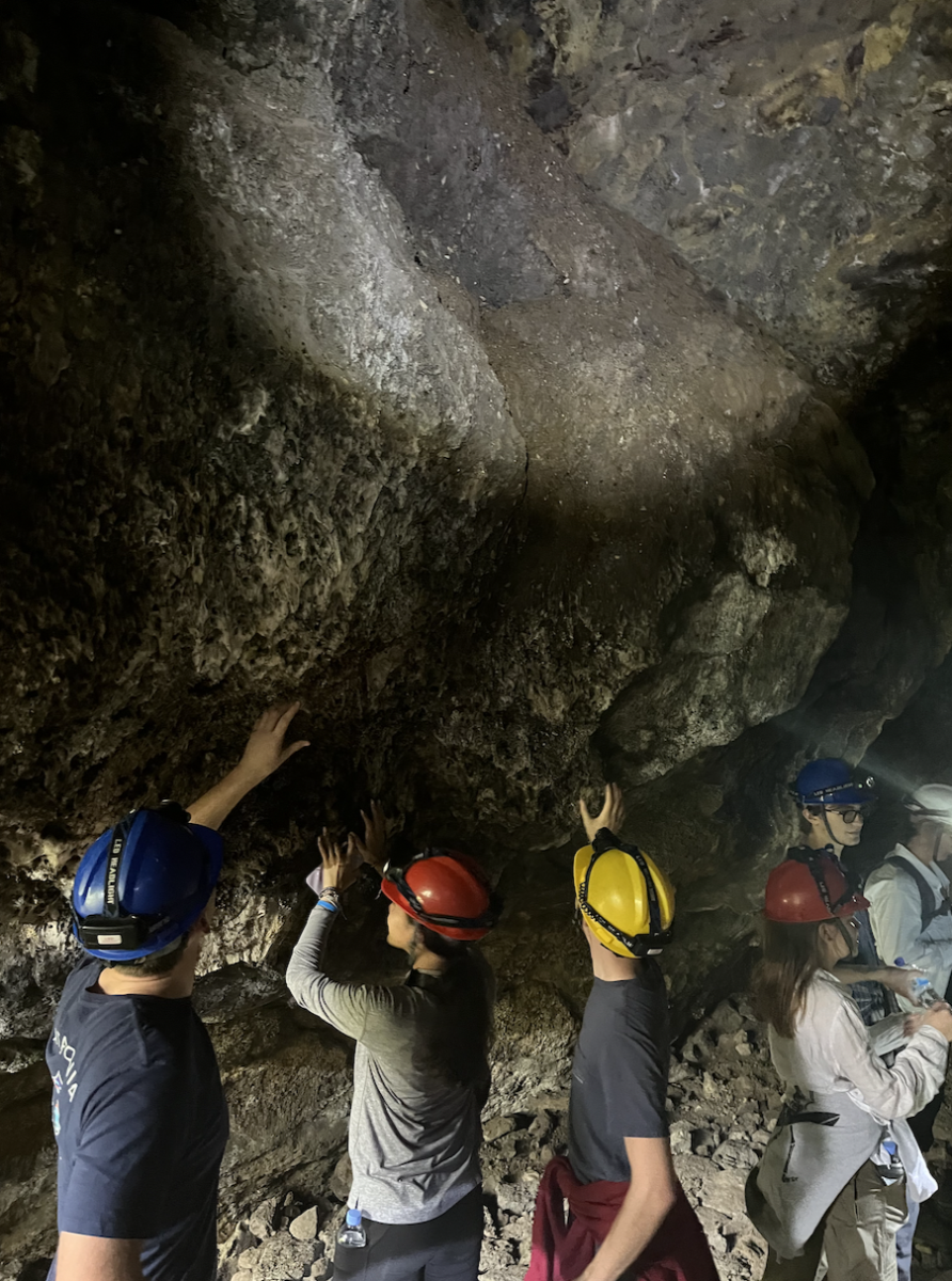 Student Ambassadors examine rock formations along the walls of a cave. The cave depicted is one of many that are part of the complex Musanze system. In order to protect themselves from hitting their heads on rocks, students and chaperones wore brightly colored hard hats with flashlights attached.