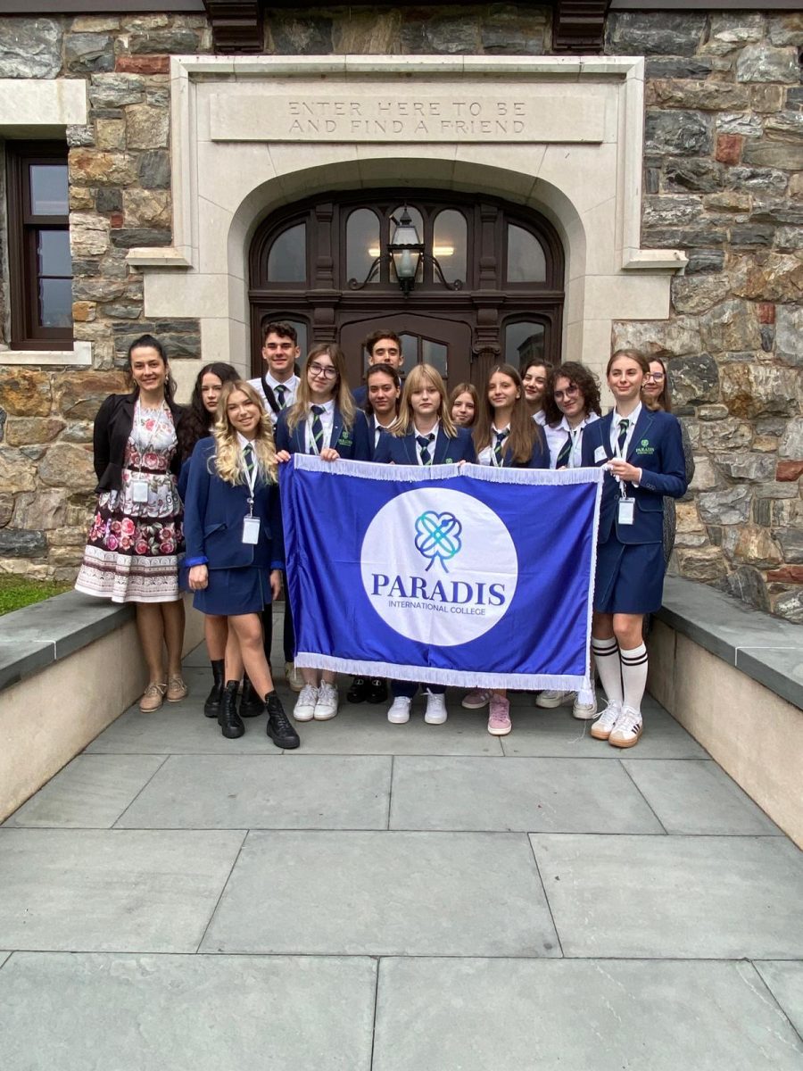 All 12 students and their teacher gathered on the Quad. They are all in their uniforms with a banner representing their school; Paradis International College. They are standing under the sign "Enter here to be and find a Friend", representing the joining of the two schools.