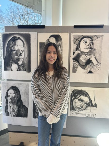 Isabella Barriera stands in front of her AP art portfolio. Her concentration is clowns, and she uses charcoal in her artwork to depict herself and friends as clowns. She uses charcoal because it encourages the viewer to look at the person rather than the colors in the art.