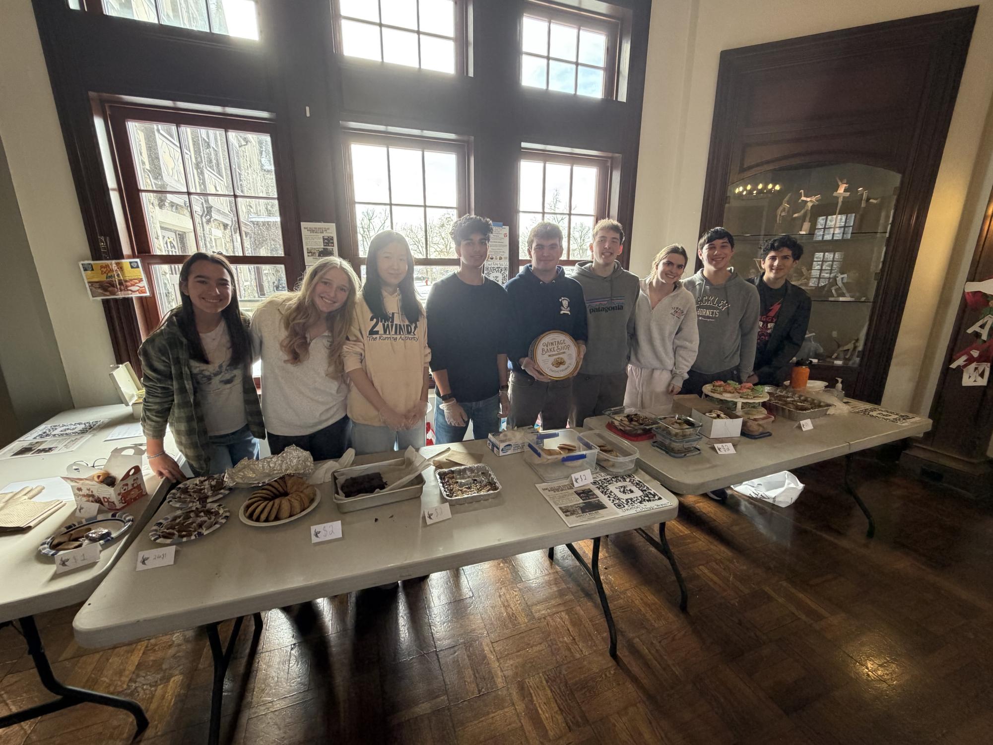 Community Council (Norah Mott, Cornelia Gruenberg, Isabelle Cai, Shikkar Misra, Peter King, Owen Spencer, and Ace Perez; left to right) & Service Leadership (Kate Masters and Tyler Stern; second and third from the right, respectively) hosted the table for the middle and upper school sales, with baked goods from over 20 Upper School students, including 17 council members, and multiple faculty members.